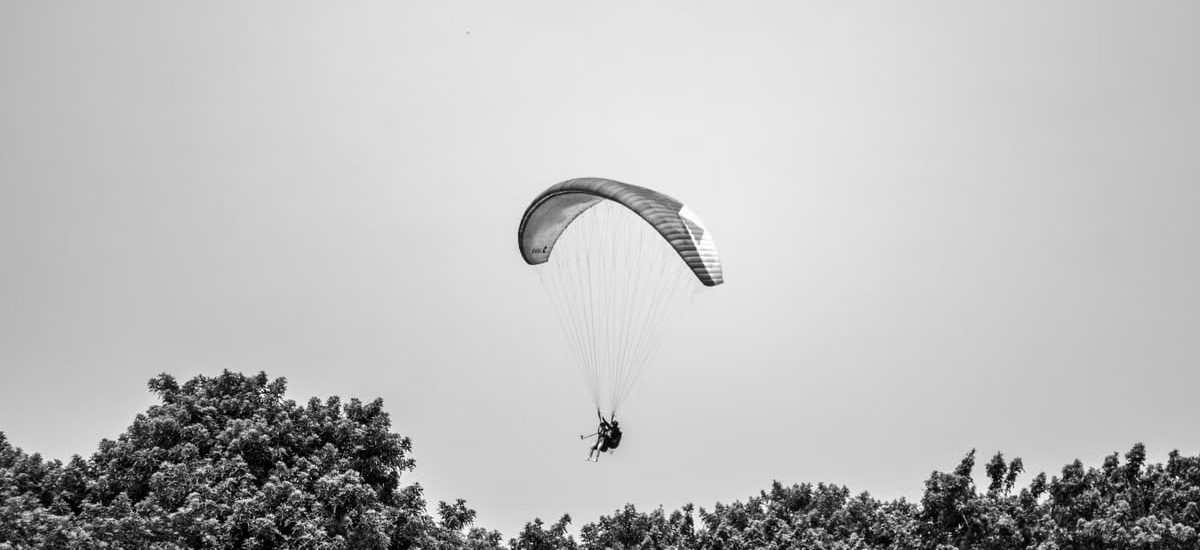 A paraglider gracefully glides above the lush trees in Lima, Peru, under a cloudless sky.