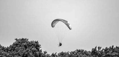 A paraglider gracefully glides above the lush trees in Lima, Peru, under a cloudless sky.