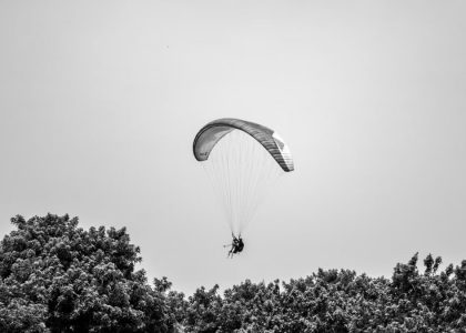 A paraglider gracefully glides above the lush trees in Lima, Peru, under a cloudless sky.
